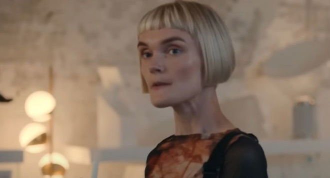 a woman with short blonde hair is standing in a room and looking at the camera .