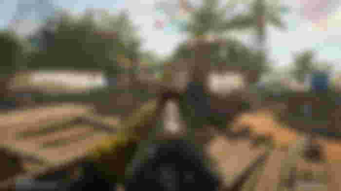A screenshot of XDefiant gameplay showing the player aiming at an enemy in the distance in a small, tropical town.
