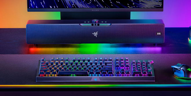 Image of a black soundbar surrounded by RGB lighting sat at a desk with a monitor, keyboard, and mouse.