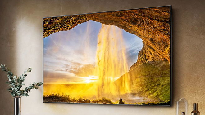 A near-frameless TV mounted to a wall with a sunset shining into a cave image on the display.