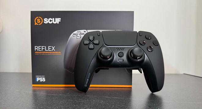 A black customized SCUF PS5 controller in front of its box, which features orange trim.
