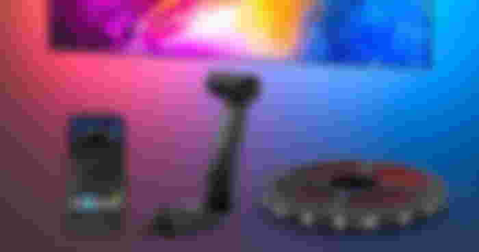 A strip of LED lights in a circle next to a black stand and phone, all of which is below a TV featuring backlighting.
