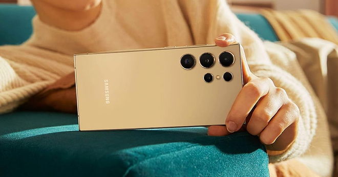 Someone in a light cream jumper holding a similarly-coloured phone with multiple cameras on the back of it.