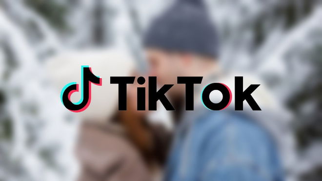 TikTok logo over a blurred background of a couple kissing in a snowy setting, related to the trending term "snowball kiss."