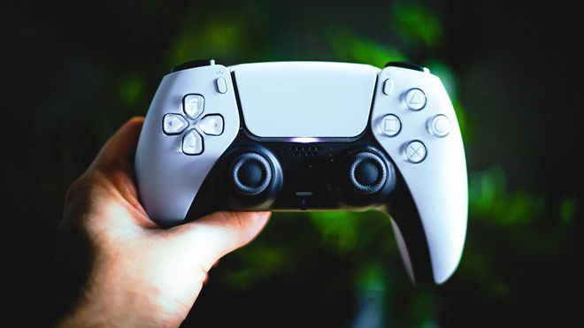 PlayStation 5 controller in a persons left hand, in front of a green background.