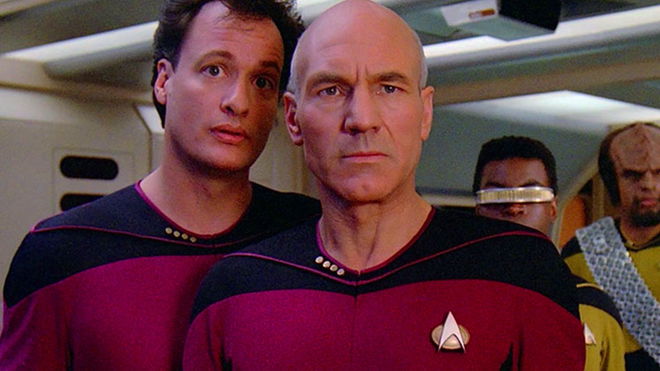 Q and Picard on the Enterprise D bridge with a communicator badge on their chest