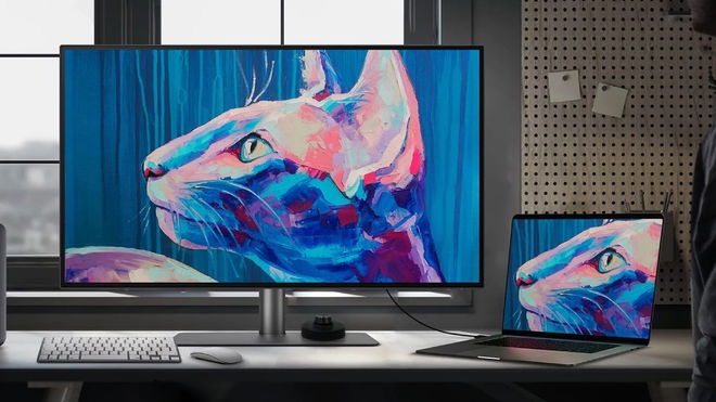 A large monitor with a cat painted in pink, blue, and purple on the display next to a thin laptop with the same image on it.