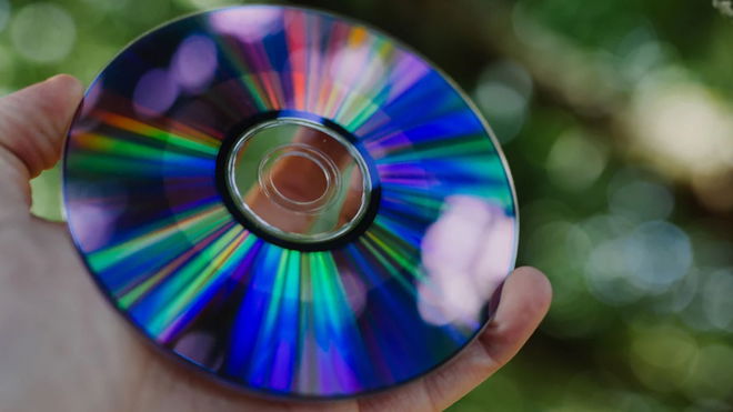 A hand holding an optical disc in front of an out of focus tree 