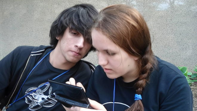 A 2008 image of two friends, a black-haired male and a brunette female, playing the Nintendo DS outside 