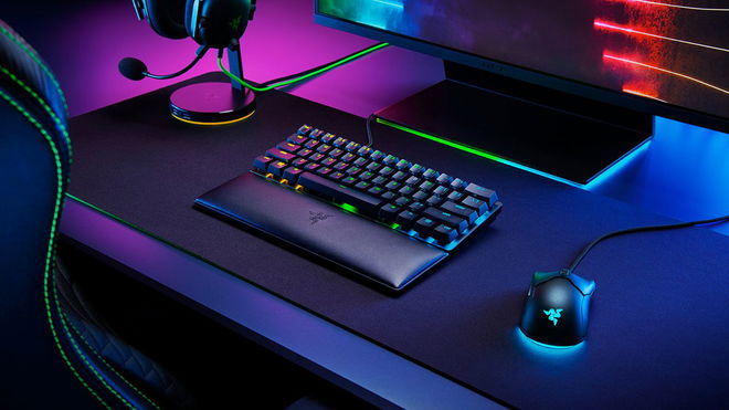 A black wrist rest in front of a black keyboard with multicoloured backlit keys, all next to a wired mouse featuring light blue lighting.