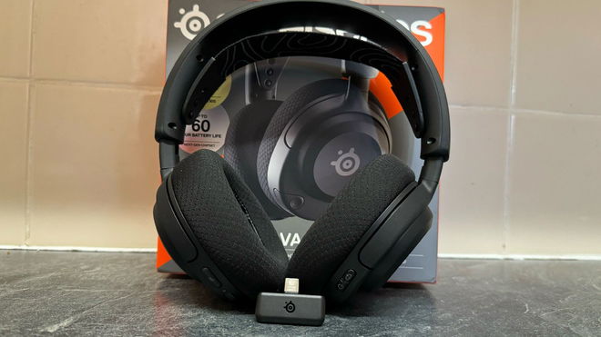 A pair of SteelSeries Arctis Nova 5 headphones in front of the box on a kitchen marbled counter