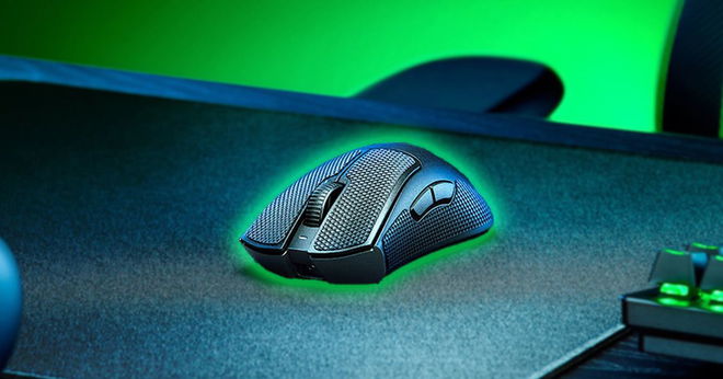 A black wireless gaming mouse with a green glow around it sat at a black desk.