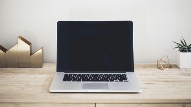 A silver laptop with a black screen and keys sat on a light wood desk.