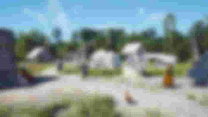 A well in Manor Lords with several tends and other structures nearby and villagers going about their day.