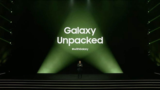 The image shows the stage setup for a Samsung Galaxy Unpacked 2024 event. The background is illuminated with a gradient of green light, focusing on the center where the words “Galaxy Unpacked” are prominently displayed in bold, white letters. 