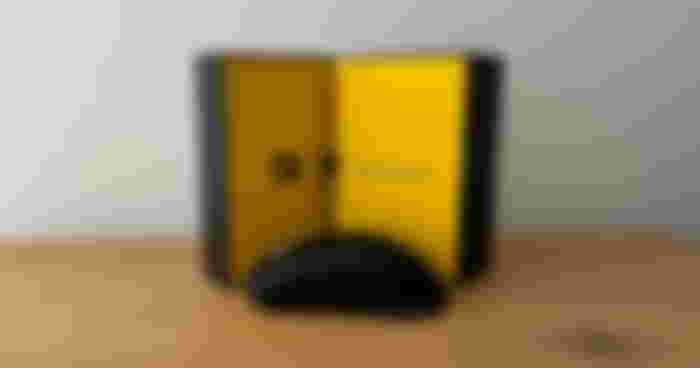 An open box with a yellow interior and a black wireless mouse sat in front of it.