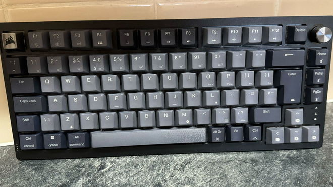 The Corsair K65 Plus Wireless keyboard in front of a tiled wall