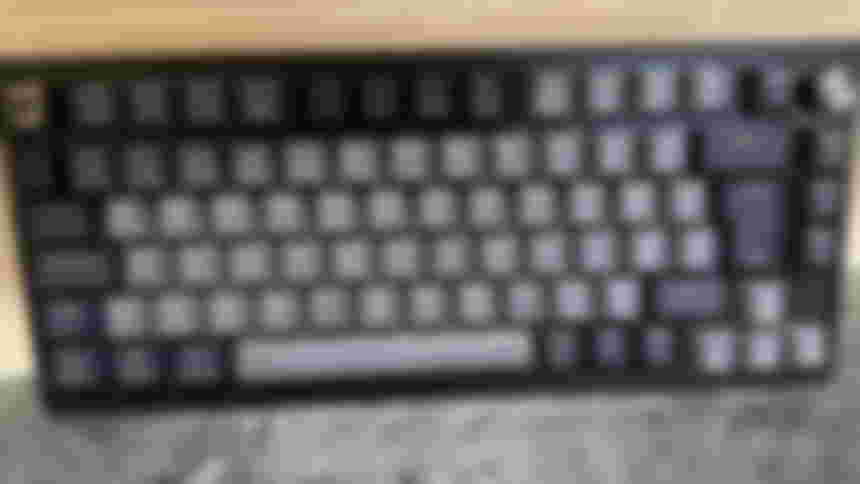 The Corsair K65 Plus Wireless keyboard in front of a tiled wall