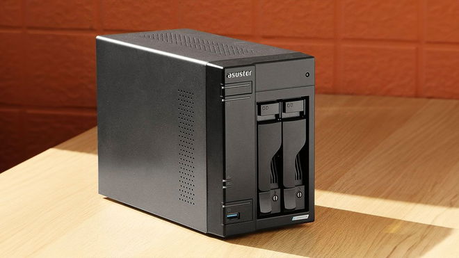 An all-black NAS device sat on a light brown wooden table in front of a burnt orange wall.