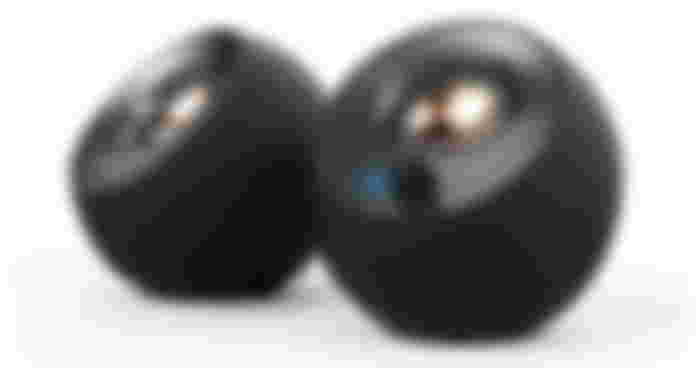 Creative Pebble v2 product image of two small, circular, black pebble speakers with bronze inner drivers.