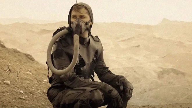 a man wearing a gas mask is sitting on the ground in the desert .