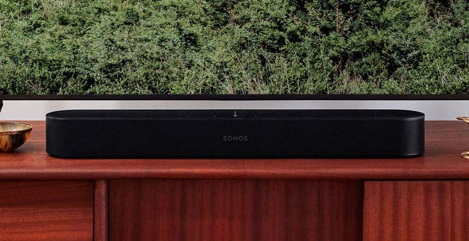 Image of a black soundbar on a brown wooden TV stand in front of a television.