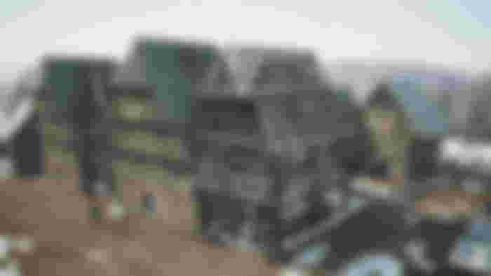 A large building under construction in Manor Lords, with several other buildings covered in snow nearby.