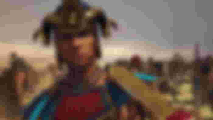 Total War Pharaoh Egyptian faction leader Amenmesse stands with sword to throat as battle rages around him.