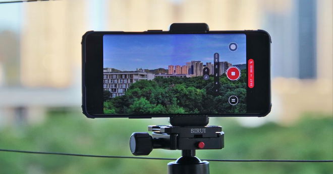 A black phone attached to a black tripod filming a city and forest landscape.