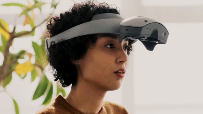 A woman with dark curly hair wearing the Sony MR headset with the top flipped up 