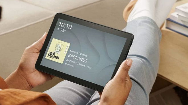 Someone in grey jeans and a brown top sitting down and looking at their black Amazon tablet.