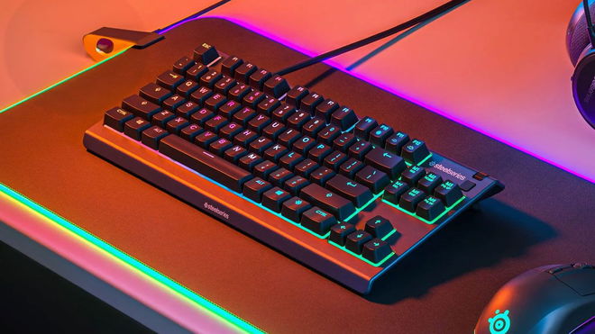 A black keyboard with purple and green backlit keys on a backlit mat and next to a black mouse.