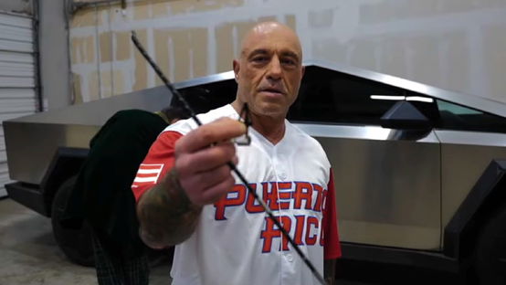 Joe Rogan holds a broken arrowhead up to the camera, after firing an arrow at a Tesla Cybertruck.
