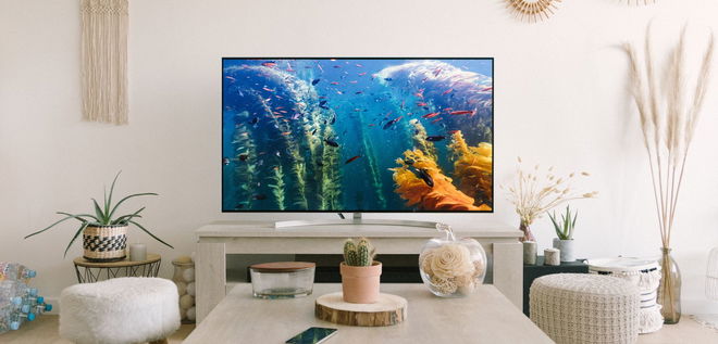 A TV with a deep sea scene on the display in a light living complete with white and cream furniture.