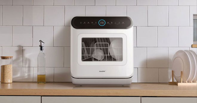 A white and black countertop dishwasher with a clear front-panel sat on a brown wooden kitchen top.