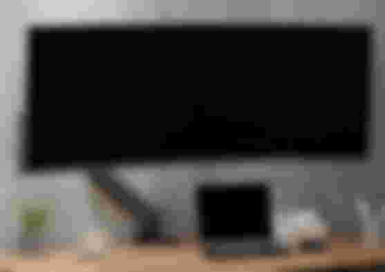 AVLT product image of a black single arm with an ultrawide monitor mounted to it and a laptop in front.