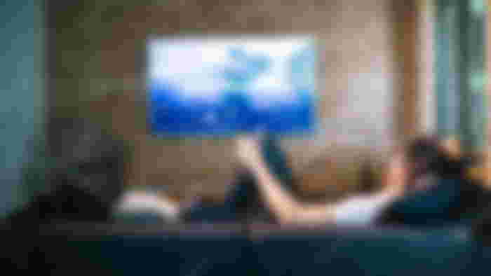 What is resolution - Someone sat on a black sofa watching a wall-mounted flatscreen TV.