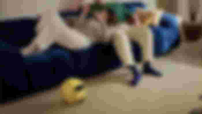 Samsung's Ballie robot on the floor beside people laying on a couch.