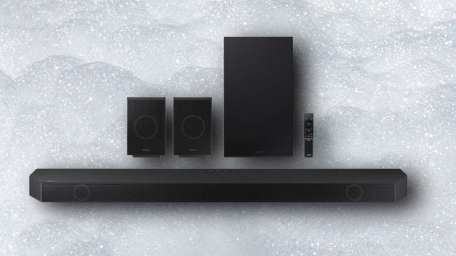 A long black rectangular soundbar with two speakers, a remote, and a subwoofer behind it.