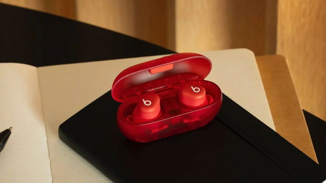 A pair of red Beats Solo Buds (2024) in their charging case, sitting on a desk and a notebook