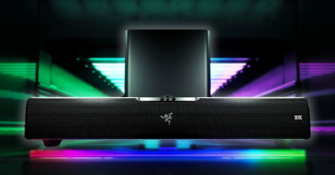 A rectangular black soundbar in front of a subwoofer, with pink, purple, and green lighting underneath it.