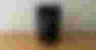 A black wireless mouse leaning against a black box while sat on a brown wood cabinet.