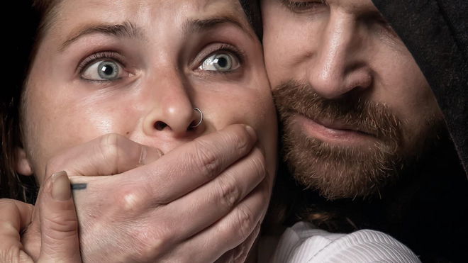 A man in a black hoodie kidnapping a woman -stock photo