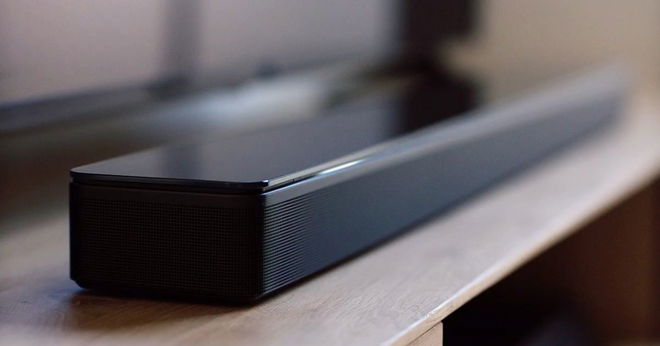 A close-up of a long black rectangular soundbar placed on top of a light brown wood cabinet.