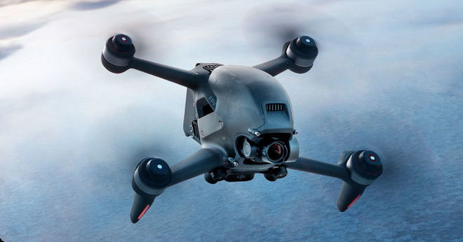 A dark grey and black four-propeller drone in flight.