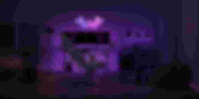 a gaming room with a chair , desk , monitors and purple lights .