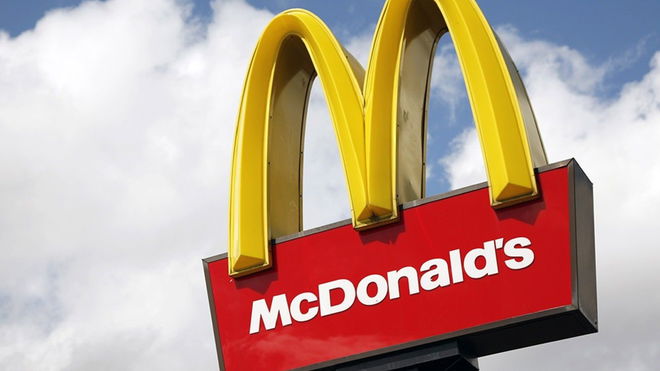 The iconic yellow arches of the McDonalds logo on a sign in front of a blue sky with clouds