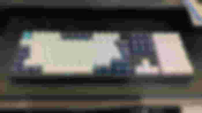 A black Keychron keyboard with white, navy, and turquoise key caps and RGB lighting behind it.