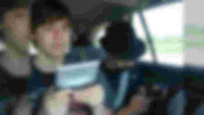 Two teenagers in the back of a car playing on the Nintendo DS in DS Download Play, one on the original silver DS and the other on a Black DS Lite