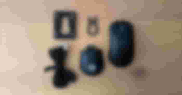 Components of a mouse next to a black wireless gaming mouse, including an alternative shell, swappable switches, and a USB cable.